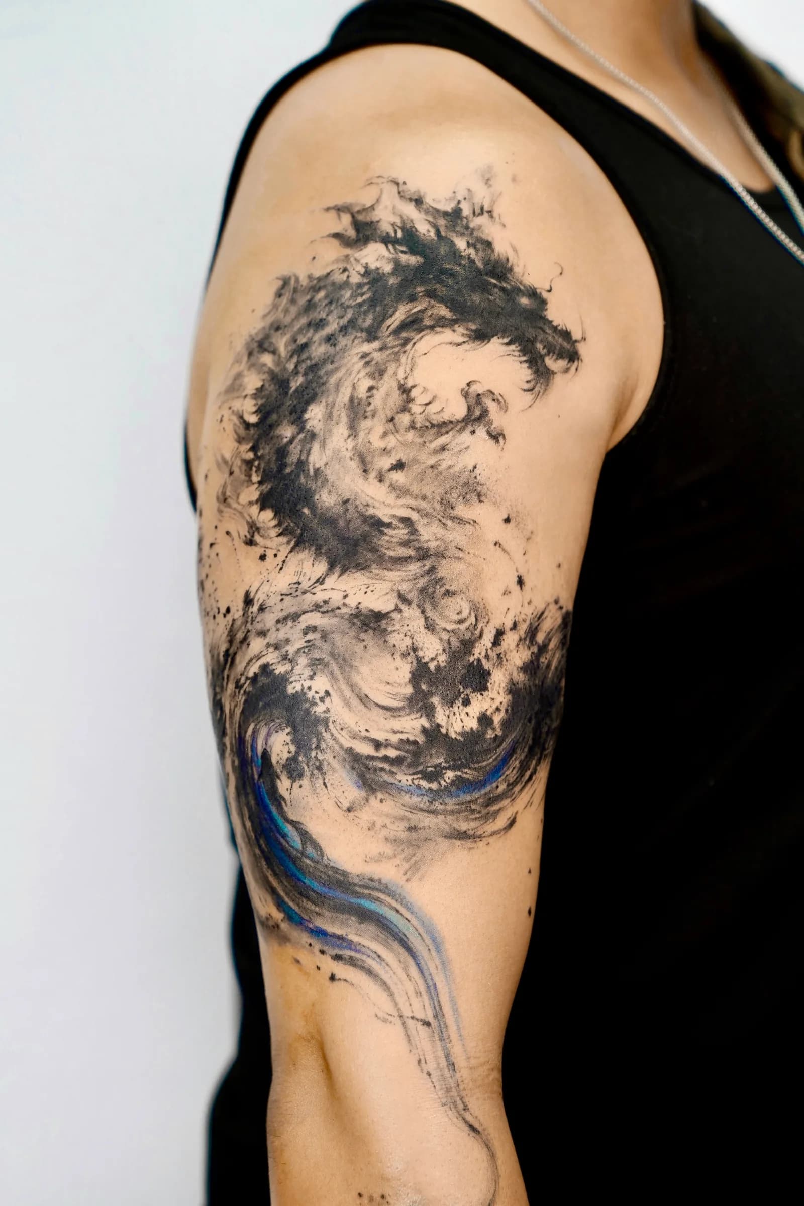 Ink-wash abstract tattoo of a rising dragon across the upper arm